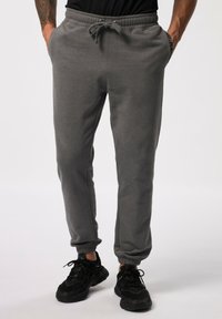 Grijze joggingsbroek met elastische tailleband, trekkoord, zijzakken en gerimpelde enkels. Stof lijkt zacht met een gladde textuur.