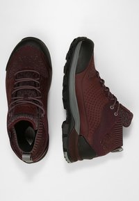 Vinröda vandringsskor med texturerat mesh och gummidetaljer. Har upphöjda prickar, en vadderad krage och hållbara, mönstrade sulor.