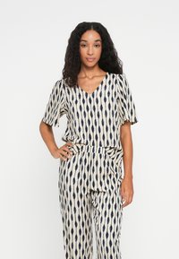 Haut à motifs et pantalon assorti en crème avec des dessins en forme de goutte allongée navy bleu. Col en V avec des manches courtes, coupe décontractée, tissu léger.