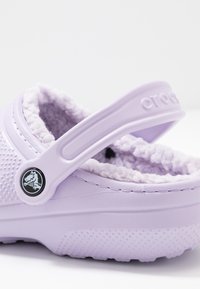 Zoccoli Crocs lavanda con tomaia testurizzata, fodera morbida e cinturino robusto. Presenta un logo circolare sul lato.