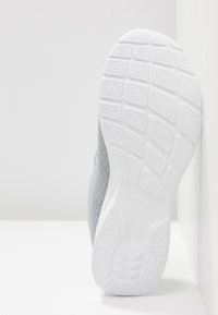 Zapatilla deportiva de color gris claro con parte superior de malla texturizada y suela de goma blanca que presenta un patrón de relieve geométrico.