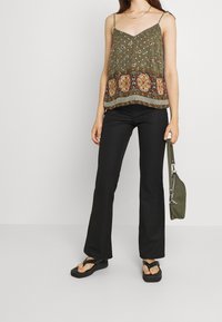 Olivgrön blommig linne med justerbara spaghettiremmar, med ett mönstrat nederkant. Matchas med svarta utsvängda byxor och svarta flip-flops.