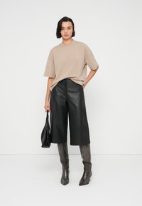 Μπεζ υπερμεγέθη κοντομάνικη μπλούζα σετ με μαύρες δερμάτινες κουλοτίνες, γκρι μπότες μέχρι το γόνατο και μια μικρή μαύρη τσάντα χειρός.