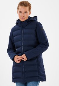 Marinblå vadderad jacka med dragkedja, hög krage och huva. Slät yta med horisontell quiltad mönstring och logotypdetalj på ärmen.