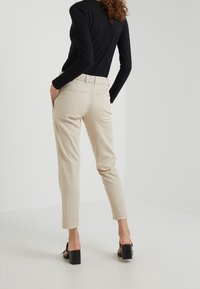 Beige broek met een taps toelopend ontwerp, gemaakt van een katoenmix. Voorzien van een tailleband met riemlussen en twee achterzakken.