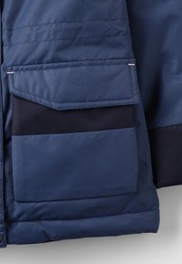 Mörkblå isolerad jacksektion med en mjuk textur, som har en stor klaffficka och en kontrasterande mörkblå detalj på fickområdet.