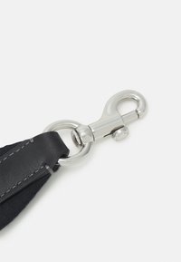 Musta nahkavyö, jossa on hopeinen metalliklipsi ja rengas, ja reunassa näkyvä ompelu yksityiskohtana lisäämään tekstuuria.