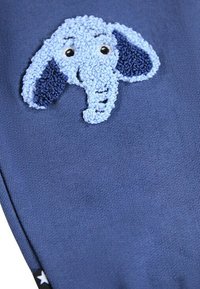 Blauwe stof met een geborduurde olifantenkop, voorzien van gestructureerde oren en gezichtsdetails in lichtblauw en zwarte accenten.