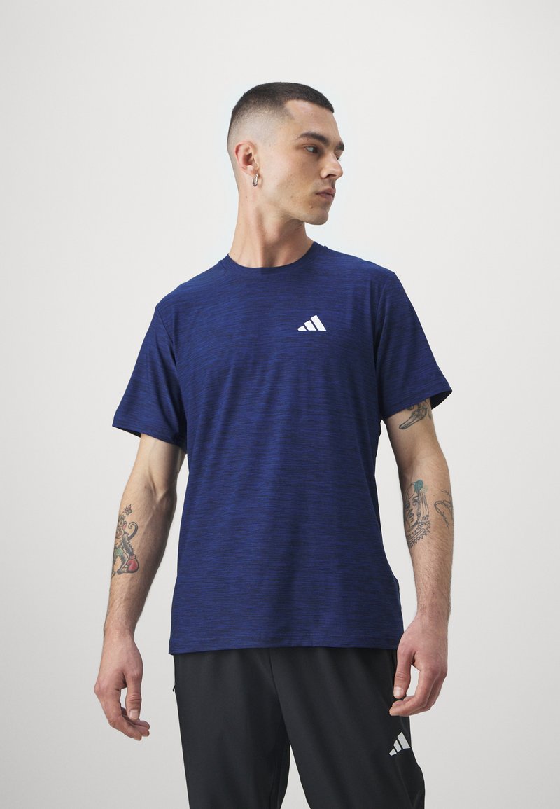 Navy blue short-sleeve athletic t-shirt made of textured fabric with a white Adidas logo on the left chest. Worn with dark pants.