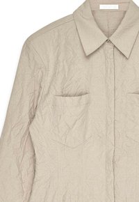 Beige gekreukt overhemd met knopen en een klassieke kraag, twee voorzakken en een gestructureerde stof. Heeft een subtiele glans en een zachte textuur.