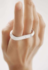 Anillo de plata con un diseño suave y curvado, adornado con tres pequeños acentos transparentes. Se lleva en un dedo con textura de piel natural.