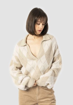 Knit sweater with a V-neck and oversized sleeves, featuring a tan diamond pattern on a light beige background. Textured, soft fabric.