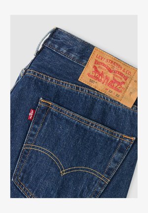 Vaqueros Levi's de mezclilla azul oscuro con bolsillo trasero visible, costuras amarillas, etiqueta roja de Levi's y etiqueta de cuero marrón de la marca con detalles de tallas.