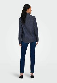 Tumman farkkukankaan paita, jossa on kärjellinen kaulus, pitkät hihat ja nappihaaltiat, yhdistettynä slim fit -tummiin farkkuihin ja mustiin korkokenkiin.