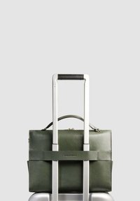 Donkergroene leren aktetas bevestigd aan een zilveren kofferhandvat met een dubbele telescopische handgreep tegen een effen grijze achtergrond.