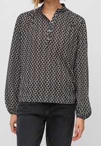 Blusa a maniche lunghe bianco e nero con motivo floreale, colletto abbottonato e tessuto leggermente trasparente. Vestibilità ampia con polsini arricciati.