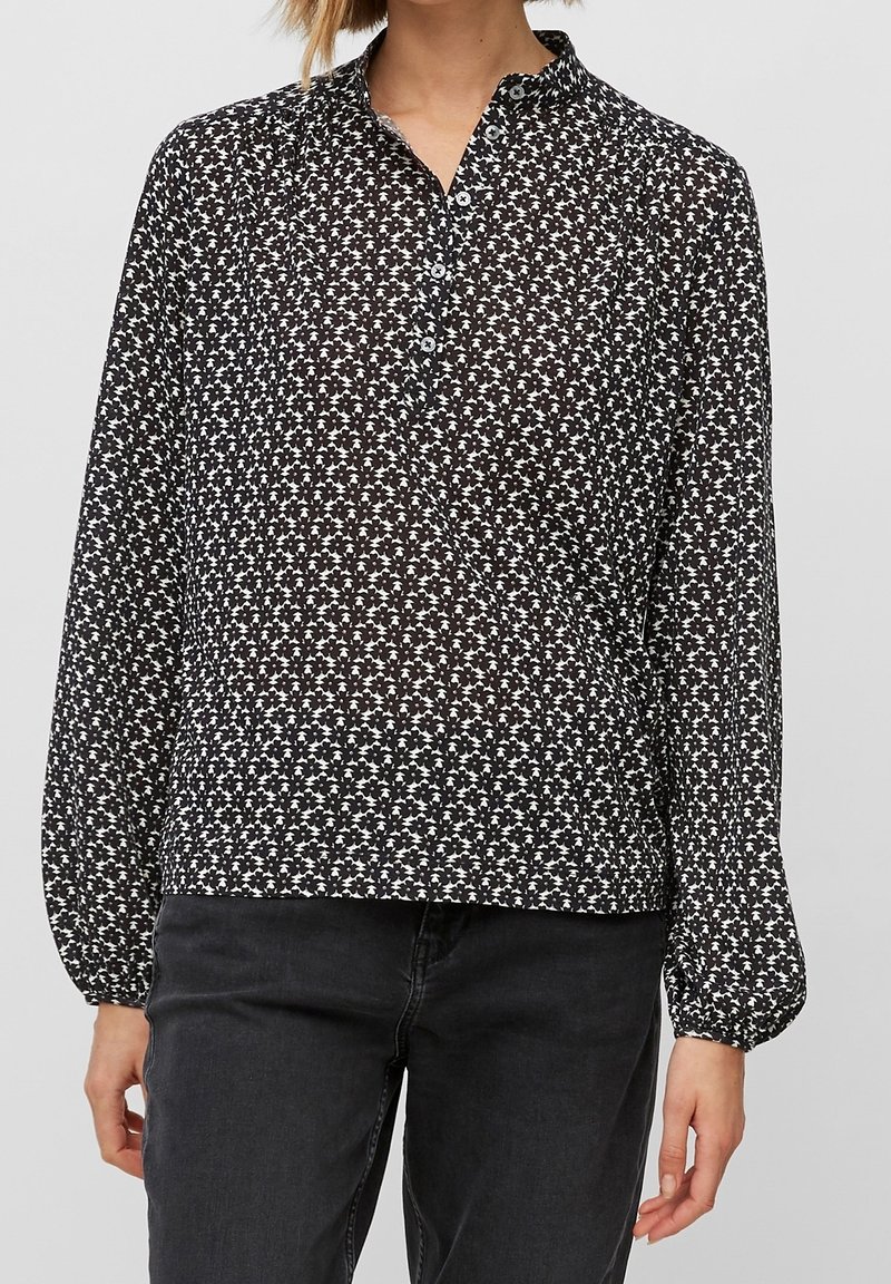 Blusa a maniche lunghe bianco e nero con motivo floreale, colletto abbottonato e tessuto leggermente trasparente. Vestibilità ampia con polsini arricciati.