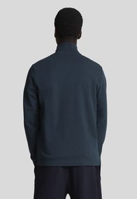 Polo a maniche lunghe blu scuro con colletto alto, tessuto texturizzato e vestibilità comoda, mostrato da dietro. Nessun logo visibile.