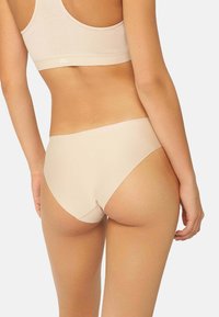 Intimo beige senza cuciture con un design a gamba alta e una texture morbida, caratterizzato da uno stile minimalista e senza cuciture visibili.