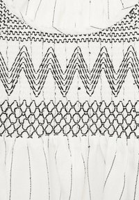 Țesătură albă cu broderie neagră, având motive în zigzag și hexagonale. Suprafață texturată cu secțiuni adunate sub design.