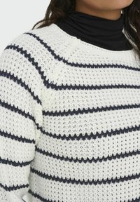 White knit sweater with navy horizontal stripes, featuring a textured open weave and a classic crew neckline.