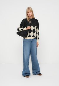 Fekete és krém színű argyle kötött pulóver, oversize fazon; világoskék, magas derekú, bő szabású farmernadrággal és fekete válltáskával párosítva.