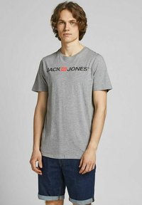 Graues T-Shirt mit kurzen Ärmeln und einem schwarzen und roten "JACK & JONES" Logo auf der Brust, kombiniert mit Jeans-Shorts. Standard Schnitt und aus Baumwolle.