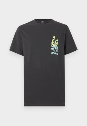 Homme portant un t-shirt noir avec un motif floral abstrait bleu et jaune dans le dos, associé à un short en jean gris clair.