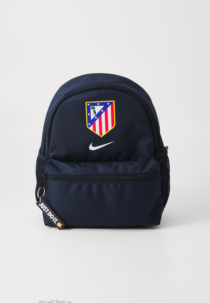 Mørkeblå ryggsekk laget av slitesterkt stoff, med et tydelig Atletico Madrid-logo, en glidelåsfrontlomme og et "Just Do It"-merke.