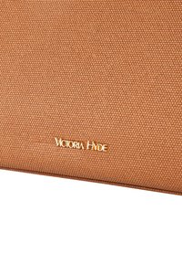 Matériau texturé beige avec un motif tissé, arborant un logo doré "Victoria Hyde". La forme est rectangulaire avec des lignes nettes.