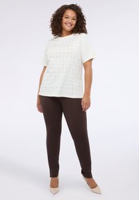 Camiseta blanca de manga corta con pequeños puntos negros, combinada con pantalones ajustados marrones y tacones beige de punta. Textura suave en general.