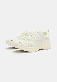 Scarpe sportive bianche in rete con dettagli testurizzati, una suola imbottita e lacci tono su tono. Presentano un manico sul tallone per facilitare l'indossamento.