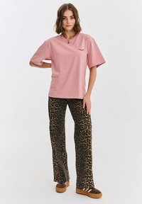 Růžové bavlněné tričko s krátkým rukávem a designem oka; spárováno s hnědými kalhotami s leopardím potiskem; model má na sobě hnědé platformové boty.