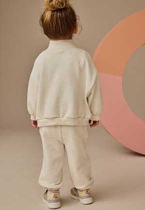 Lys creme sweatshirt- og buksesæt med flerfarvede sprøjt, blød tekstur, løs pasform, ribbede manchetter, parret med farverige sneakers.