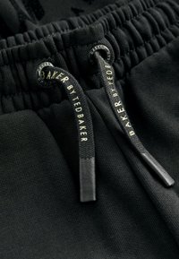 Primer plano de una cinturilla elástica negra con cordones negros que presenta el texto "BAKER BY TED BAKER" en blanco.
