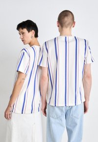 T-shirts à manches courtes avec des rayures horizontales rouges, bleues et blanches. Le tissu semble doux ; coupe décontractée avec un col rond classique.