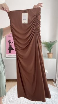 Vestido midi marrón, con fruncidos y hecho de una tela suave. Presenta una etiqueta lateral y un diseño drapeado, que muestra textura y una silueta suave.