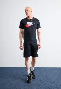 Črna Nike majica s barvitim logotipom, črne kratke hlače, bele crew nogavice in črne teniske. Gladek material, športen kroj, preprost dizajn.