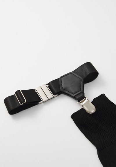 Sort justerbar rem med en glat læderpatch, sølvmetal hardware og tekstureret stofdetalje i den ene ende.