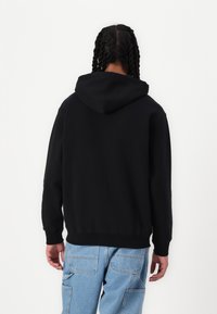 Svart hettegenser med ribbestrikkede mansjetter og hem, med en romslig hette og en avslappet passform, brukt med lyseblå jeans.