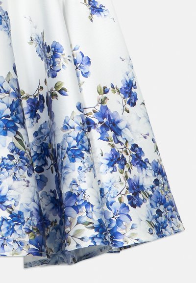 Λευκή φούστα με μπλε floral σχέδιο και πράσινα φύλλα, εμφανιζόμενη σε απαλές πτυχές πάνω σε ένα απλό λευκό φόντο.