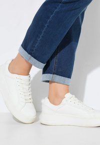 Białe sneakersy o gładkiej fakturze i delikatnych detalach w postaci szwów. W zestawieniu z podwiniętymi ciemnymi dżinsami z jasnoniebieskimi mankietami.