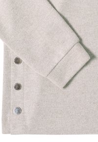 Tissu ribbed gris clair avec un détail de bouton sur le côté comportant des boutons métalliques. Le poignet de la manche a une finition lisse et simple.