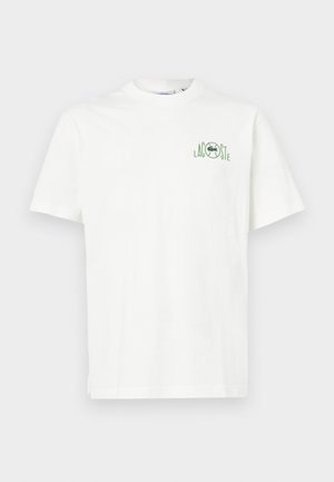 Camiseta de algodón blanca con cuello redondo y mangas cortas. Presenta un logo verde de Lacoste en la parte izquierda del pecho. Diseño simple y sin adornos.