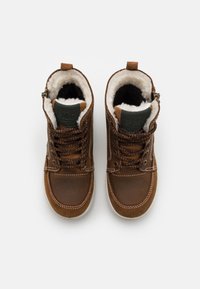 Botas de tobillo de cuero marrón con forro de pelo sintético, cordones marrones y un acento verde en la lengüeta. Suelas de goma de color claro.