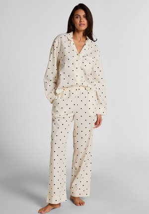 Roomkleurige pyjama set met zwarte polka dots. Het shirt heeft een knoopsluiting en een zak; de broek heeft een elastische taille en omslagboorden.