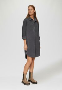 Graues Denim-Hemd Kleid mit Kragen, Brustblende und hochgerollten Ärmeln. Verfügt über einen abgerundeten Saum und seitliche Schlitz. Getragen mit klobigen braunen Knöchelschuhen.