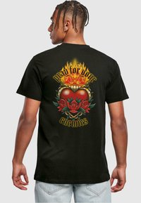 Black cotton t-shirt featuring a colorful graphic of a heart, flames, and roses, with the text "pray for your enemies" in bold lettering.