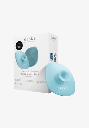 Blauwe siliconen gezichtsborstel met zuignap naast de witte verpakking met het label "SmartAppGuided Facial Brush 4 in 1" van GESKE.
