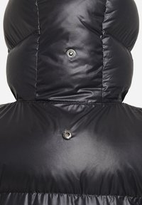 Chaqueta negra acolchada con un cuello alto, que presenta una textura brillante y un detalle de botones a presión plateados en la parte posterior.